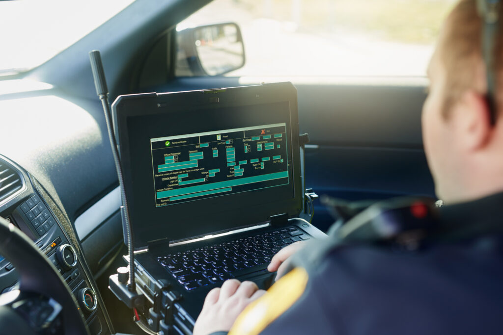 Image of a law enforcement officer using a laptop inside a patrol vehicle